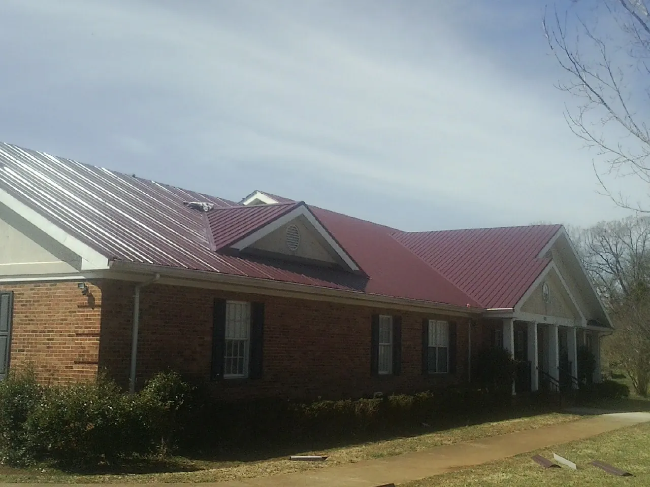 Red metal roof with gabled entries on a long brick building, from a Hail Damage Roof Repair job in Bloxom