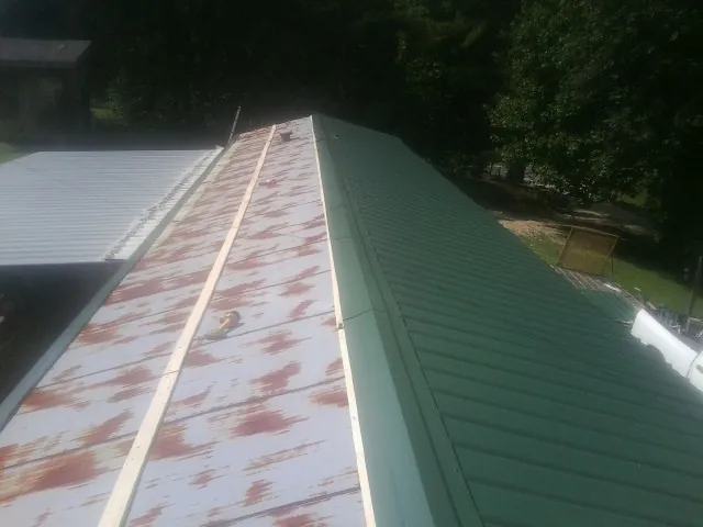Old rusted panels beside newly installed green metal roofing — Wind Damage Roof Repair by Roofing Brothers in Bloxom