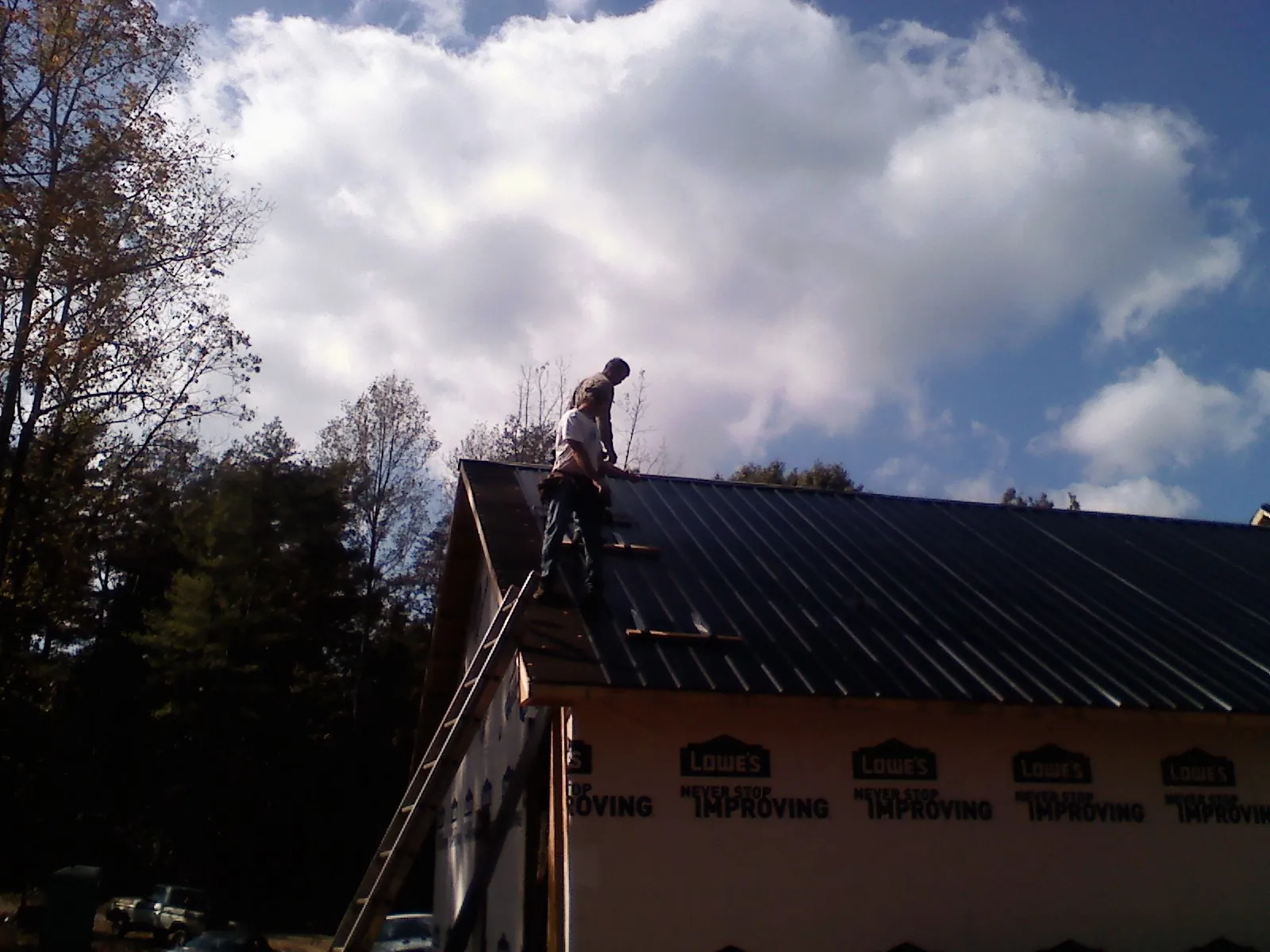 Roofer fastening dark metal panels high against a cloudy sky, from a Roof Inspection job in Bloxom