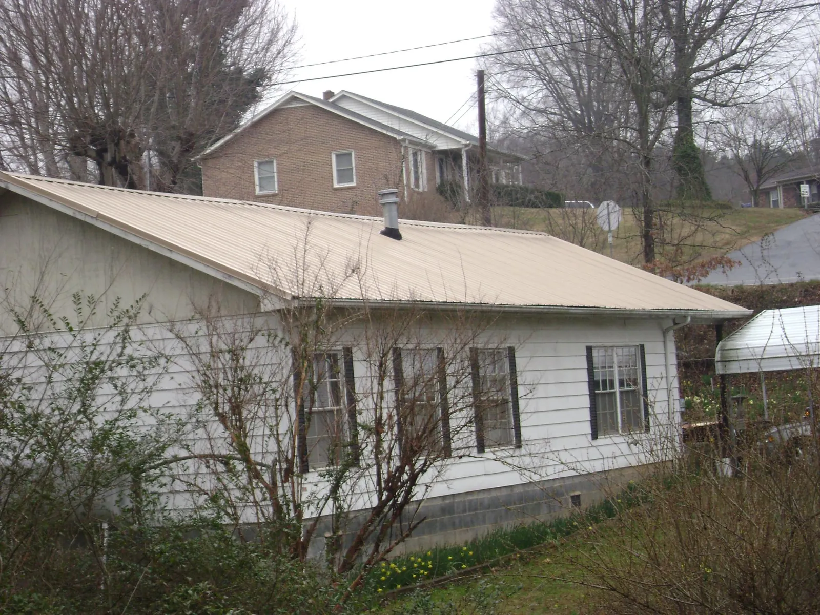 Tan metal roof on a white sided house set into a hillside — Commercial Roofing by Roofing Brothers in Bloxom